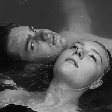 Nahaufnahme von zwei Gesichter, ein Mann und Frau, welche im Wasser treiben. Der Mann schaut zur Kamera, die Frau verträumt nach Oben.