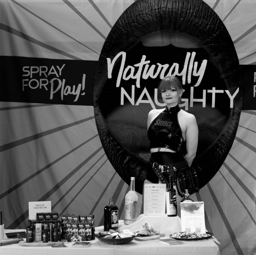 Eine Frau in Latexkostüm steht bei einem Messestand der Firma Naturally Naughty